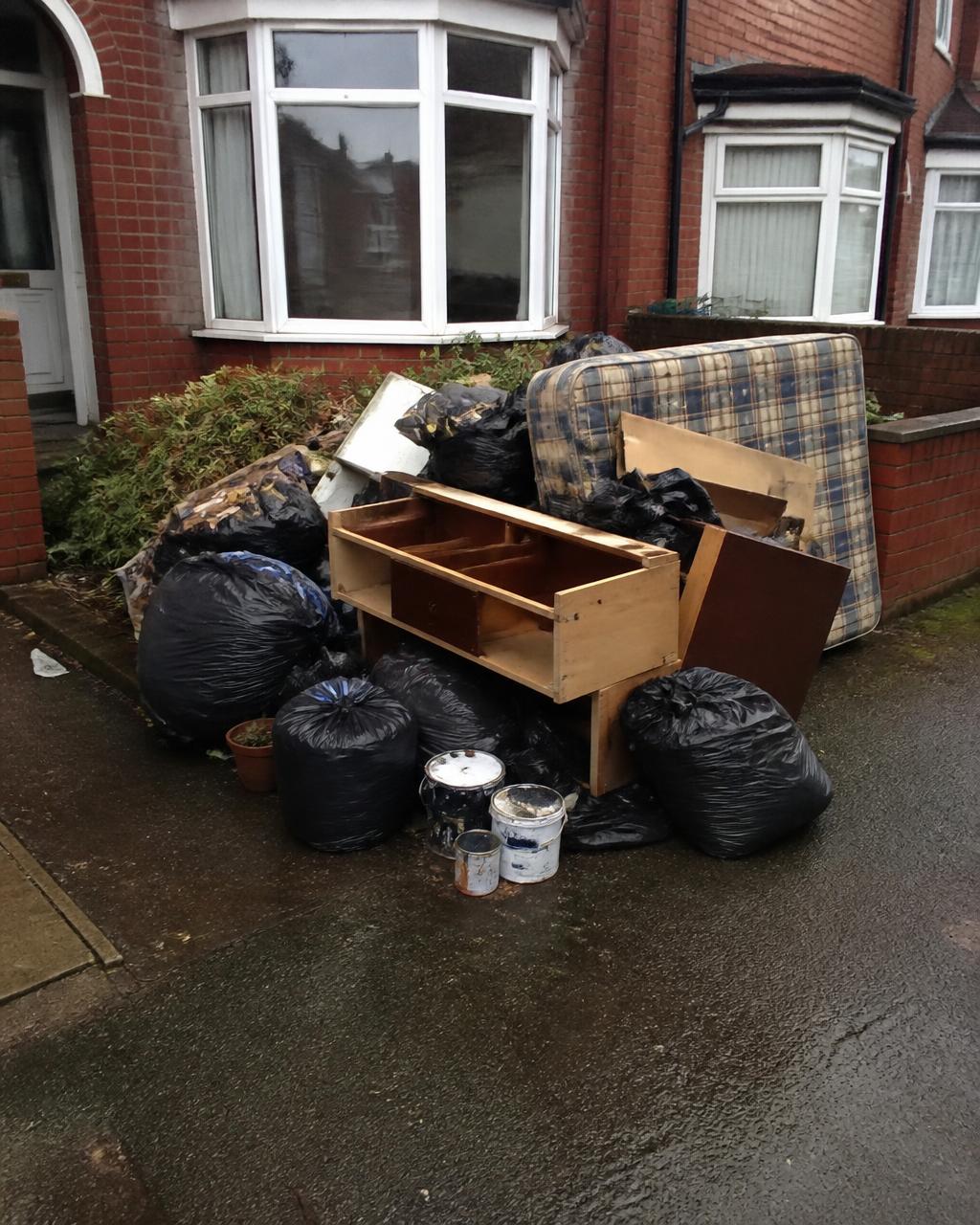 A driveway pile of bin bags, a broken chest of drawers, a mattress and paint tins